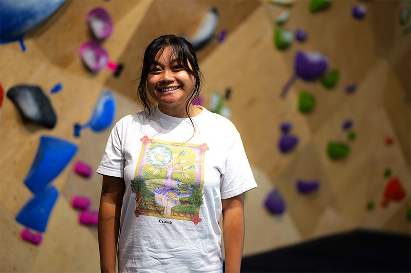 Mckayla Leonares smiling in front of a climbing wall