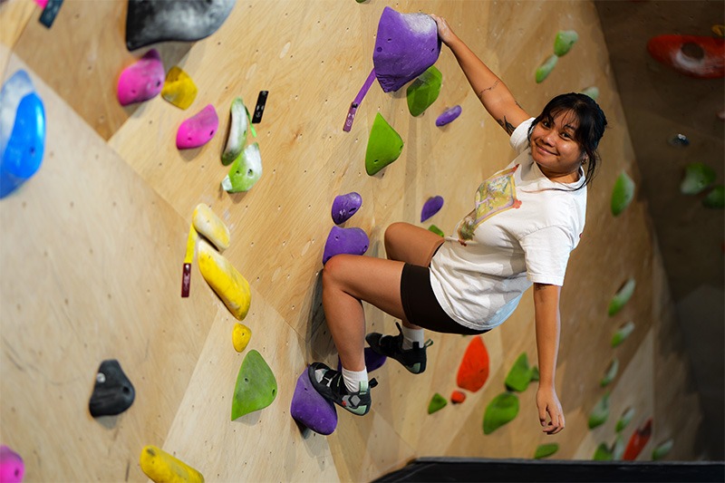 Mckayla Leonares climbing a wall and smiling
